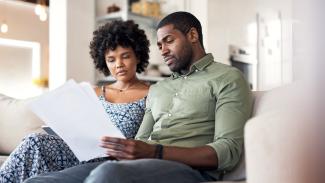 Two people sitting on a couch together as they look at a paper intently